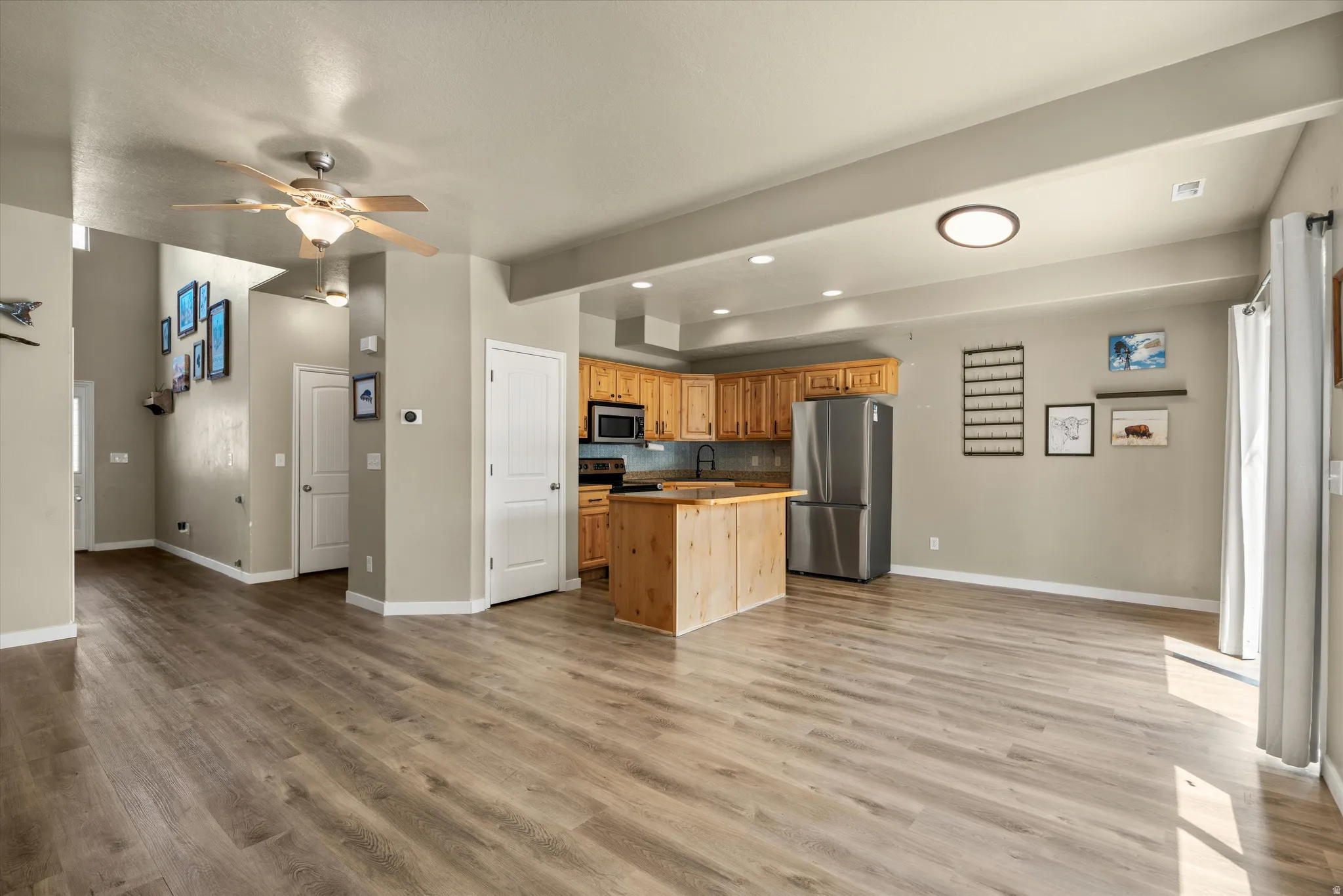 Open-concept living area with wood-finish flooring, a kitchen island, recessed lighting, and a stainless steel refrigerator