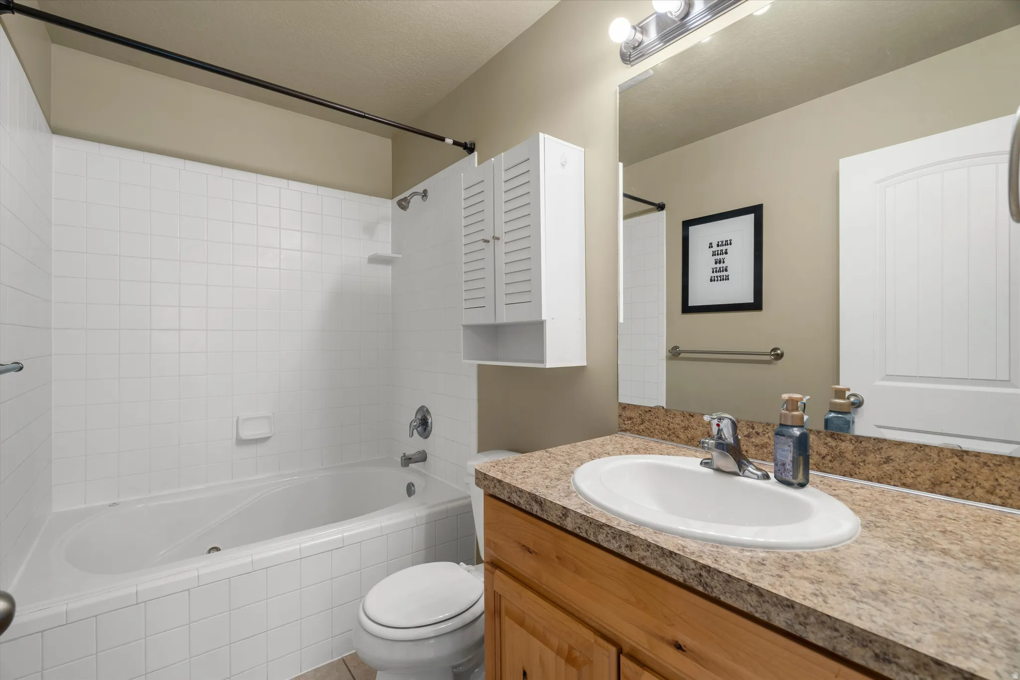 Bathroom vanity with a tan patterned countertop, oval drop-in sink, and light wood-finish cabinetry