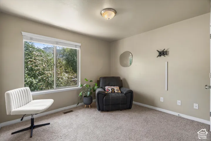 Bright room featuring a large window with white trim, tan painted walls, and light-colored carpet flooring