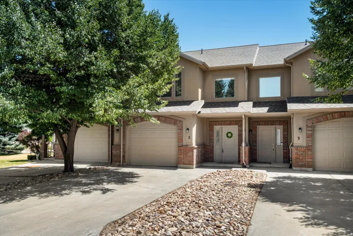 Stucco and brick facade residence featuring two entry doors with sidelights, two garage doors, and upper-level windows