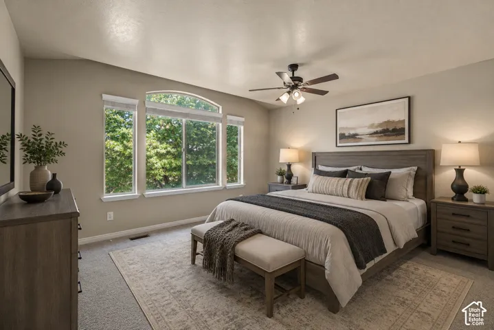 Vaulted ceiling with a ceiling fan light fixture, large arched window, wood-finish dresser, and carpet flooring
