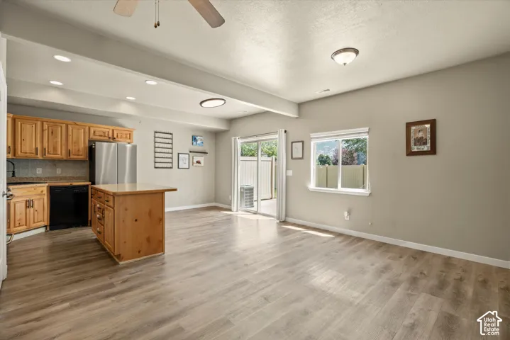 Open-concept living space with wood-finish flooring, a kitchen island, stainless steel refrigerator, black dishwasher, and sliding glass door access to an outdoor area