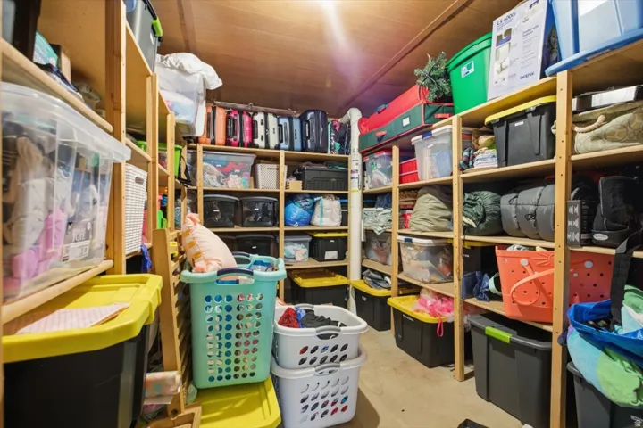 Storage area featuring extensive wood shelving, sloped ceiling, and overhead lighting