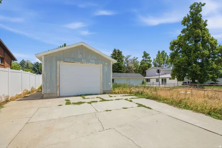 Detached garage with a paneled door, concrete driveway, and white privacy fencing