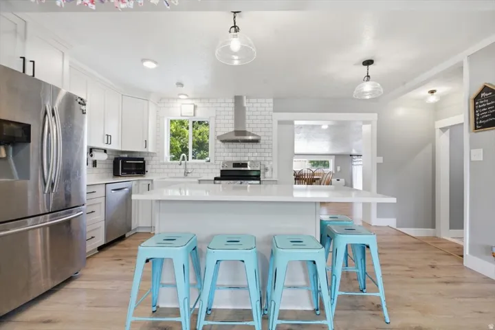 Contemporary kitchen featuring white cabinetry, subway tile backsplash, stainless steel appliances, and wood-finish flooring