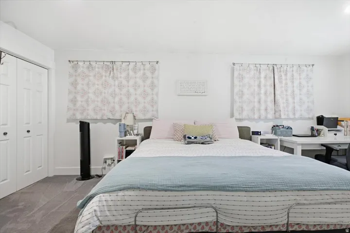 Bedroom featuring light gray carpeting, a two-panel closet with bifold doors, and two windows with patterned curtains