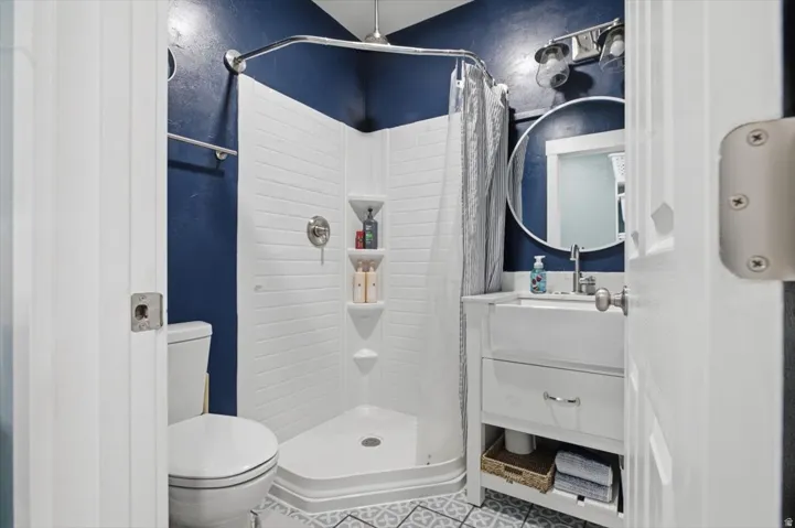 Compact bathroom featuring a corner shower with built-in shelving, a white toilet, and a vanity with an integrated sink