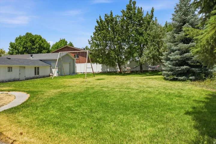 Expansive backyard featuring a manicured lawn, mature trees, and a concrete pathway