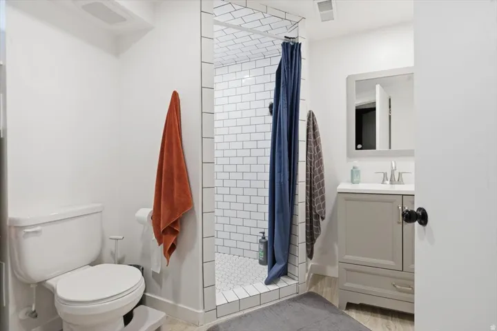 Bathroom featuring a subway-tiled shower, a white hexagonal tile shower floor, a grey vanity with a white countertop, a rectangular mirror, and wood-finish flooring