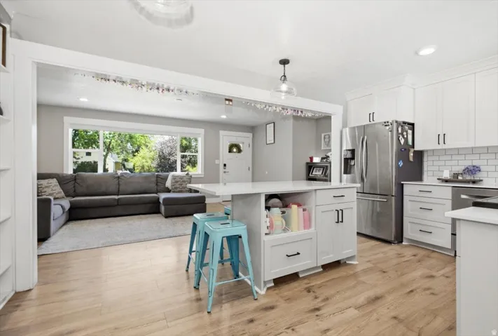 Kitchen featuring a central island with countertop seating, white shaker cabinetry, stainless steel appliances, and wood-finish flooring