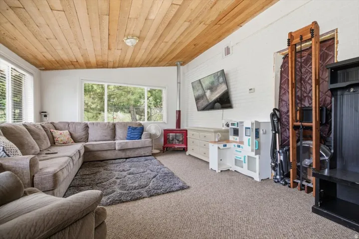 Living area featuring wood-finish plank ceiling, large windows with horizontal blinds, and a built-in wall-mounted television