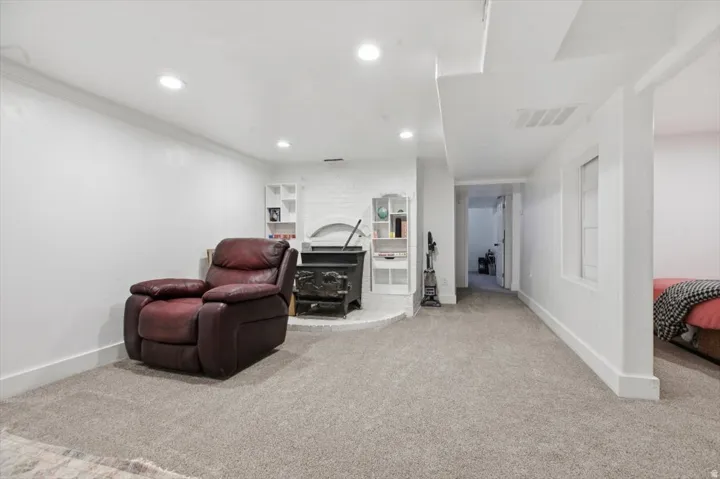 Carpeted living area featuring a prominent wood-burning stove with a hearth, recessed lighting, white built-in shelving, and white baseboards