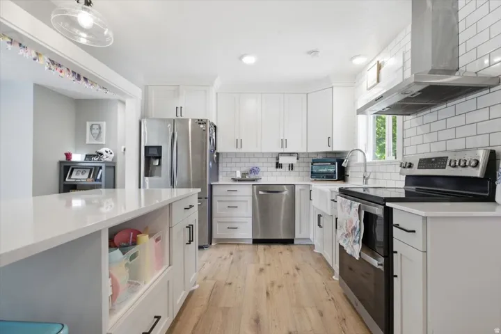 Modern kitchen featuring white shaker cabinetry, stainless steel appliances, a white subway tile backsplash, light-toned wood-finish flooring, and a large central island with a light-colored countertop