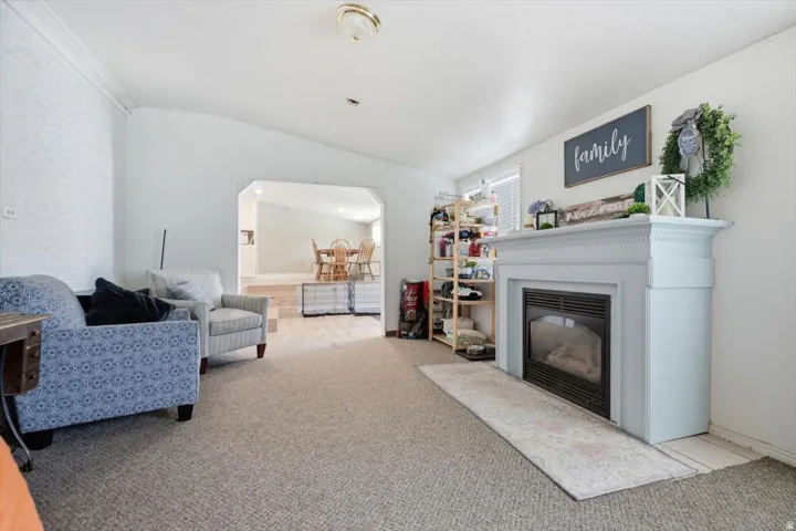Living area featuring a white mantel fireplace, light gray carpeting, and an arched opening to an additional room