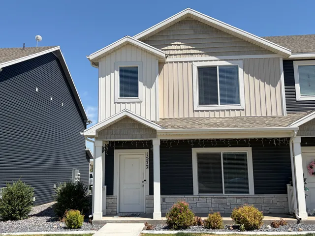 Two-story townhome exterior featuring multi-toned siding, a covered entry with stone accents, a composite shingle roof, and a concrete walkway
