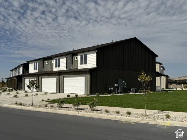 Multi-story townhome with a dark vertical siding exterior and white garage doors