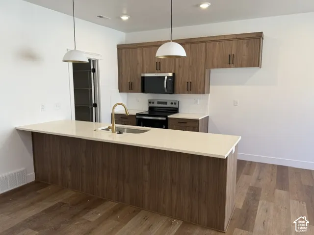 Modern kitchen featuring wood-finish cabinetry, light-toned countertops, stainless steel appliances, and a white tile backsplash