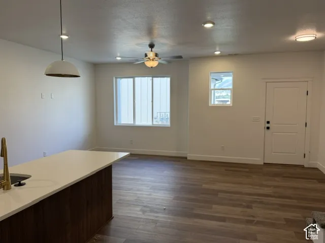 Wood-finish flooring throughout, bright white walls, recessed lighting, ceiling fan, and a kitchen island with a light-colored countertop