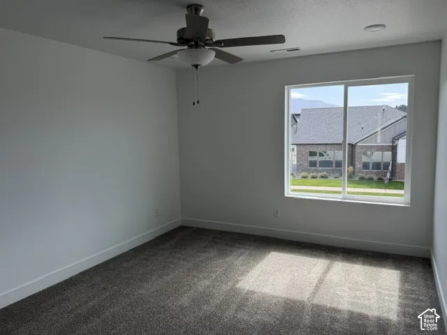 Spacious room with gray carpet, white walls, a ceiling fan, and a large window