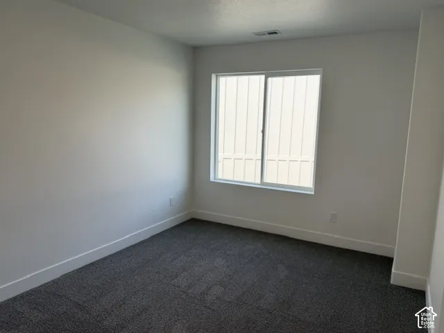 Wall-to-wall carpeting in a neutral tone, white painted walls, and a large window with vertical blinds