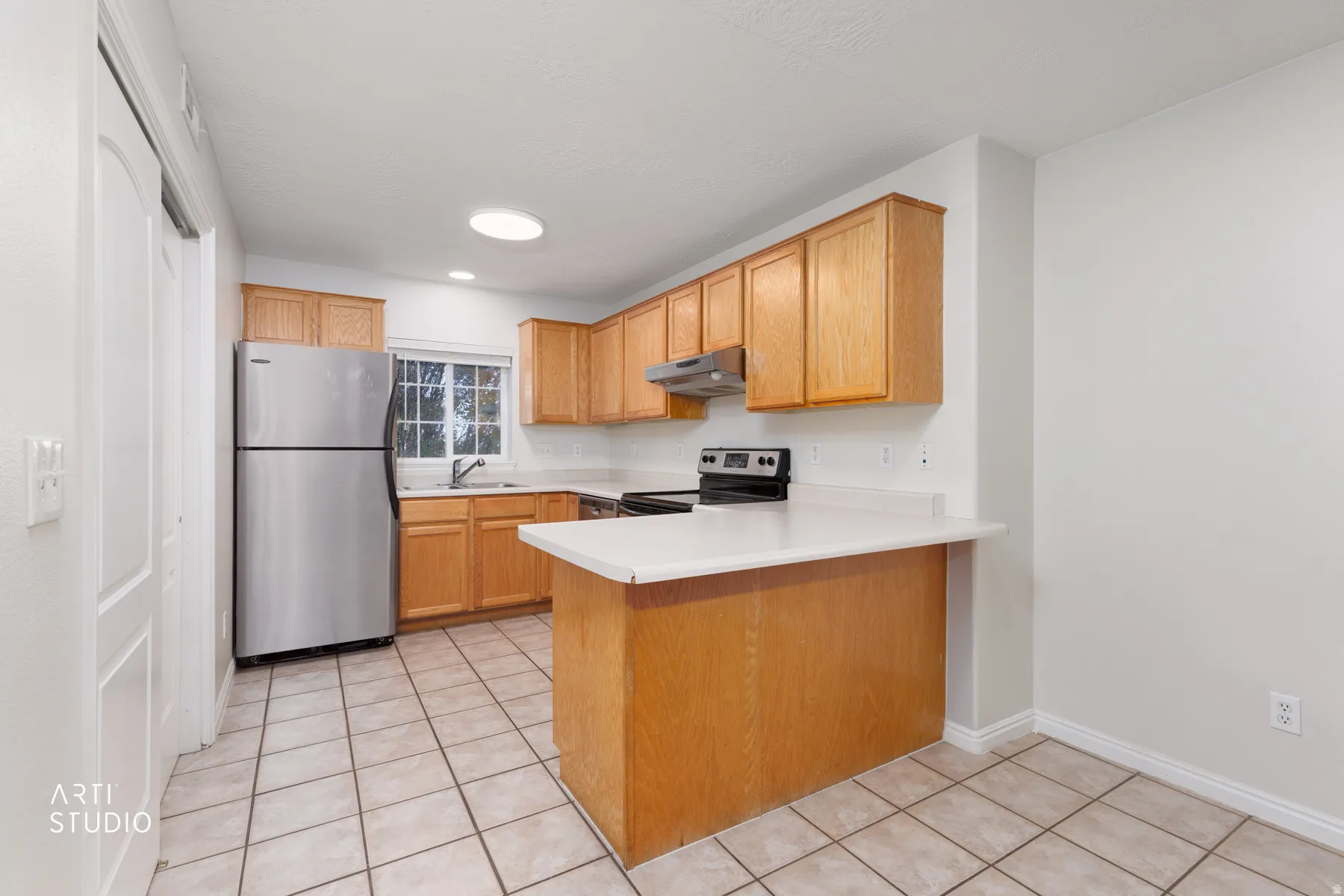 Functional kitchen featuring wood cabinetry, stainless steel refrigerator, black range, and light-toned countertops