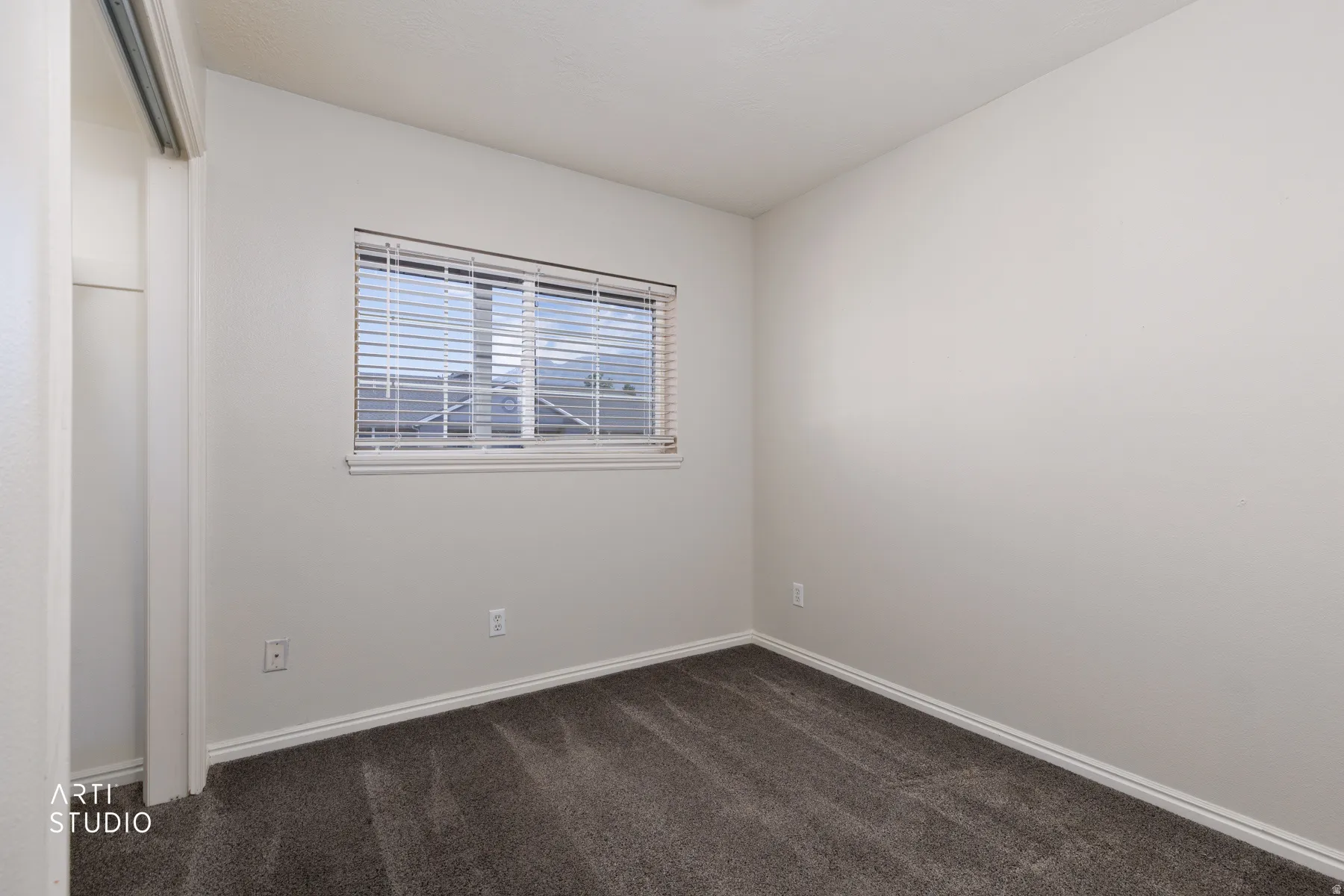 Room featuring a window with horizontal blinds, neutral wall paint, white baseboards, and dark gray carpeting