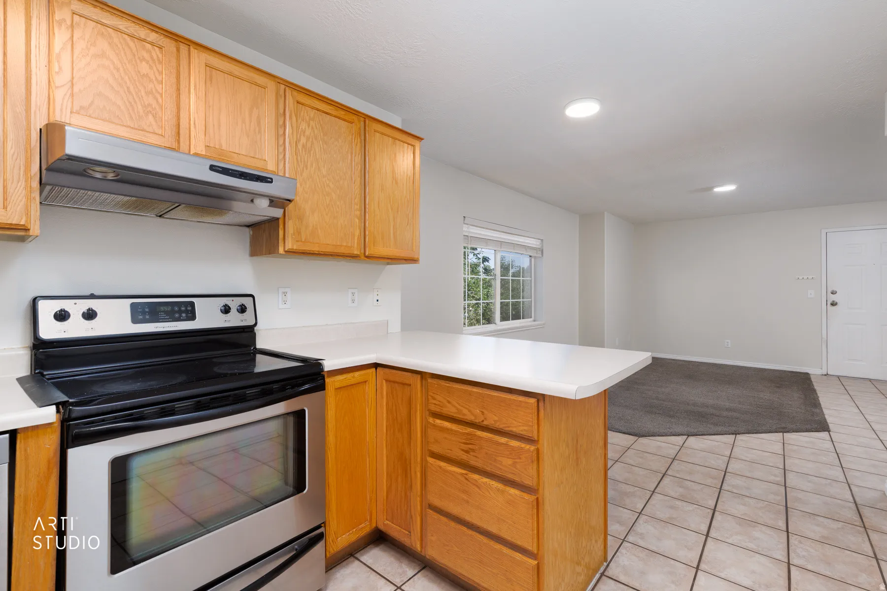 Kitchen featuring wood cabinetry, light-toned countertops, and a stainless steel oven with an overhead range hood