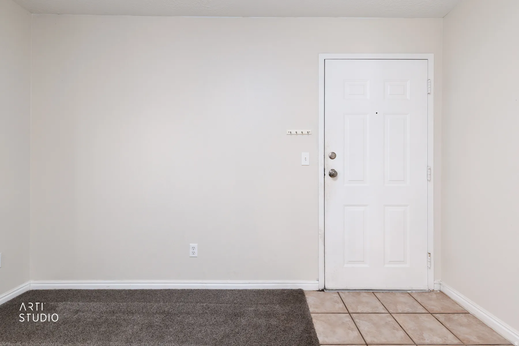 Entryway featuring a white paneled door with brushed nickel hardware, light neutral walls, and a transition from carpet to square tile flooring