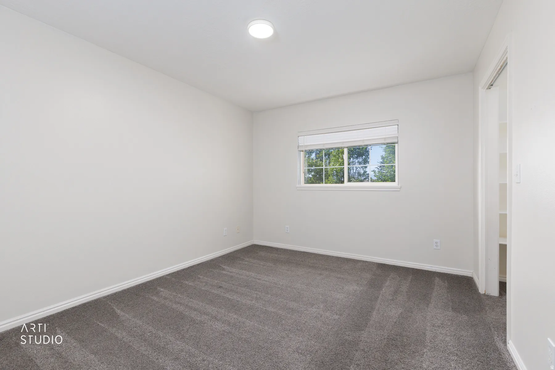 Carpeted room featuring a white ceiling with recessed lighting, white walls, and a window with a roller shade