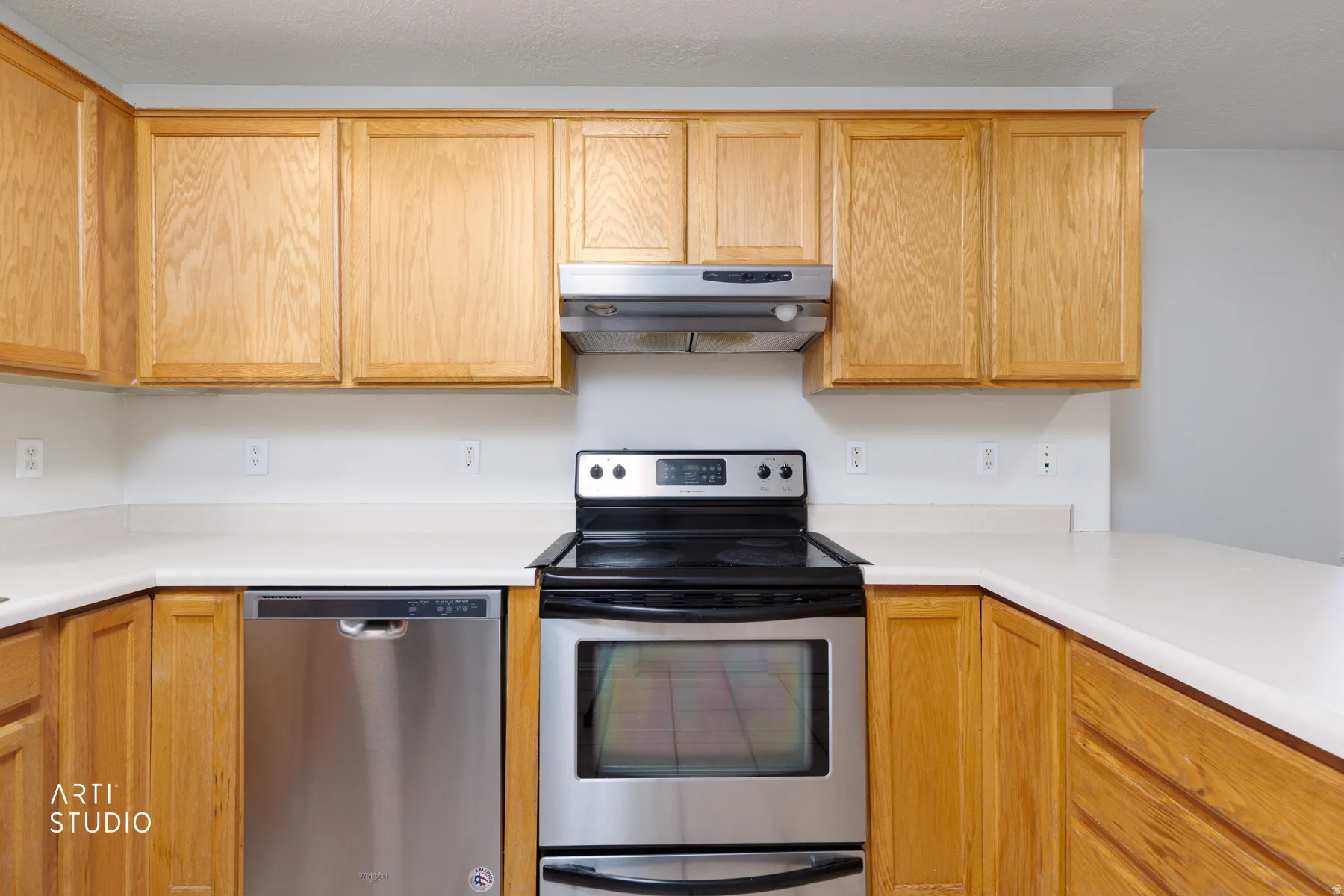 Kitchen featuring light wood cabinetry, white countertops, stainless steel electric range, stainless steel range hood, and stainless steel dishwasher