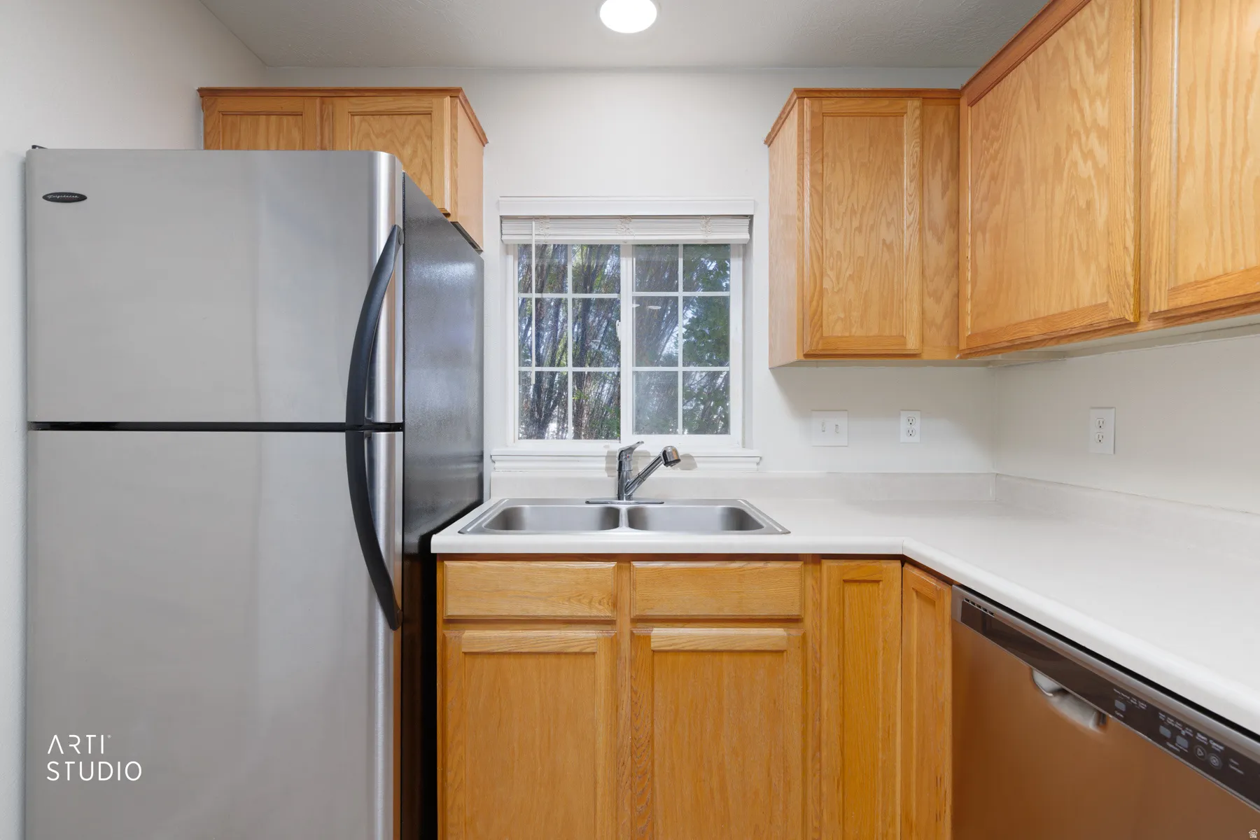 Kitchen featuring wood cabinetry, white countertops, stainless steel refrigerator, stainless steel double basin sink, and a built-in dishwasher