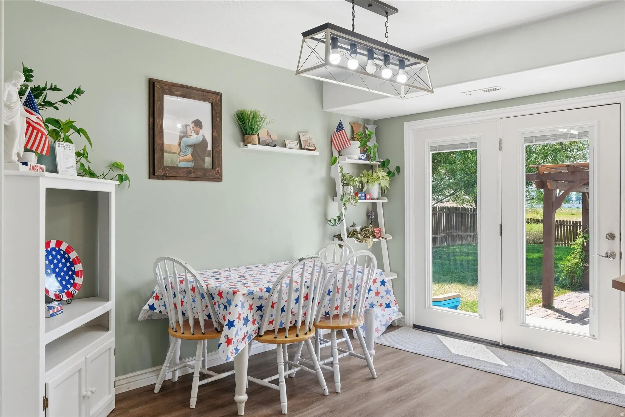 Dining area featuring wood-finish flooring, a contemporary linear chandelier, light green wall tones, and double glass-paneled doors leading to the exterior