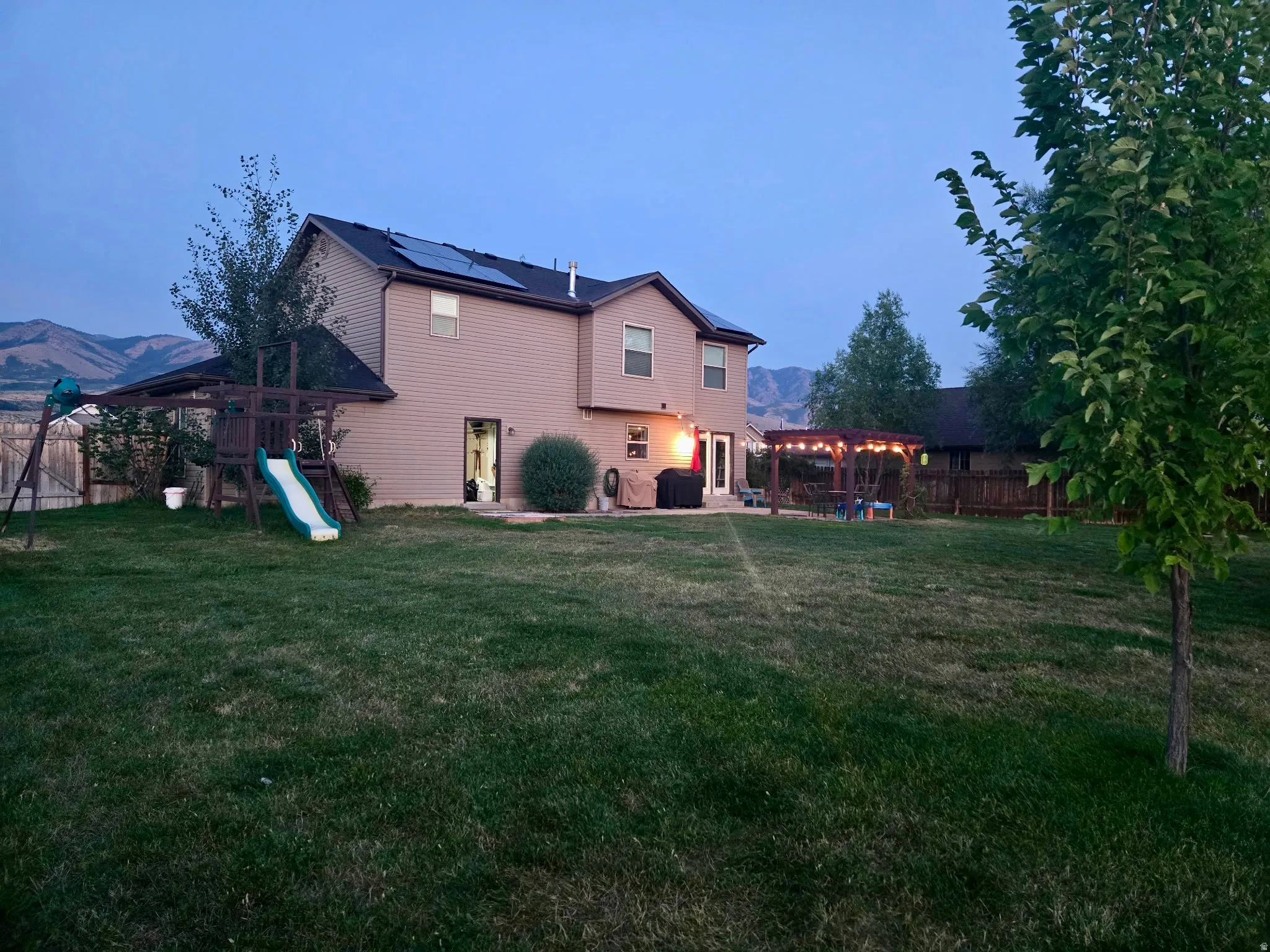 Expansive backyard featuring a large green lawn, a wooden playset, and a patio area with a pergola