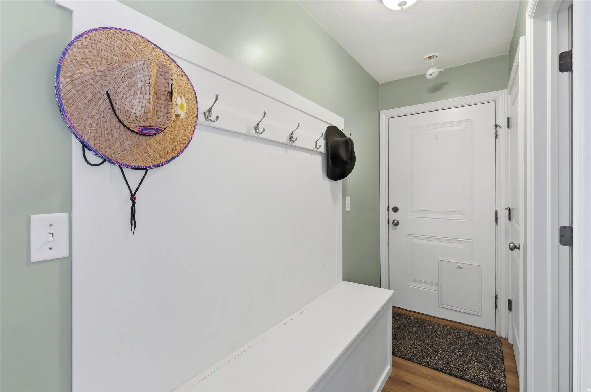 Entryway mudroom featuring a built-in bench, wall-mounted coat hooks, and durable wood-finish flooring