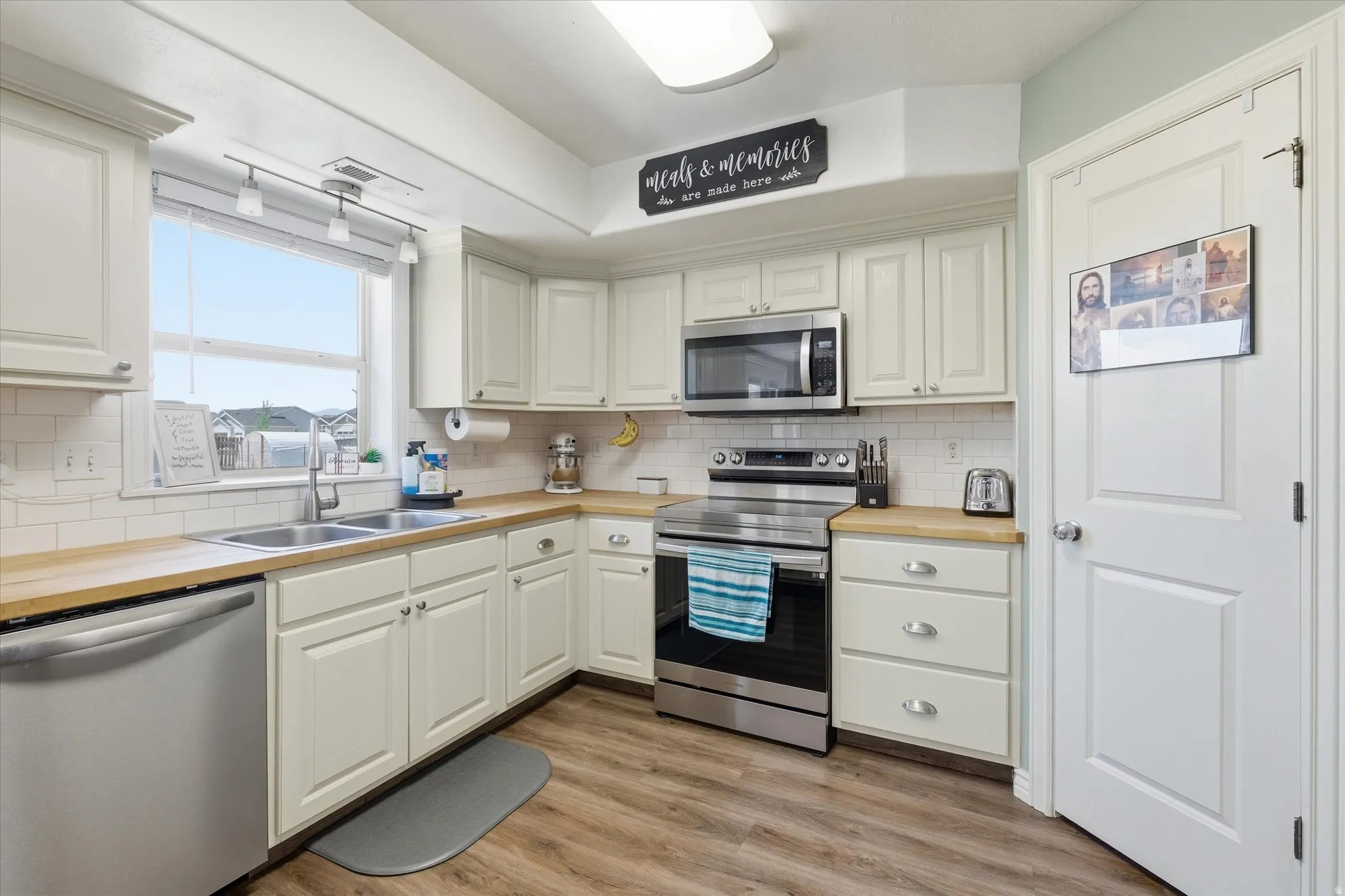 Corner kitchen featuring white cabinetry, light wood-finish countertops, stainless steel appliances, and wood-finish flooring