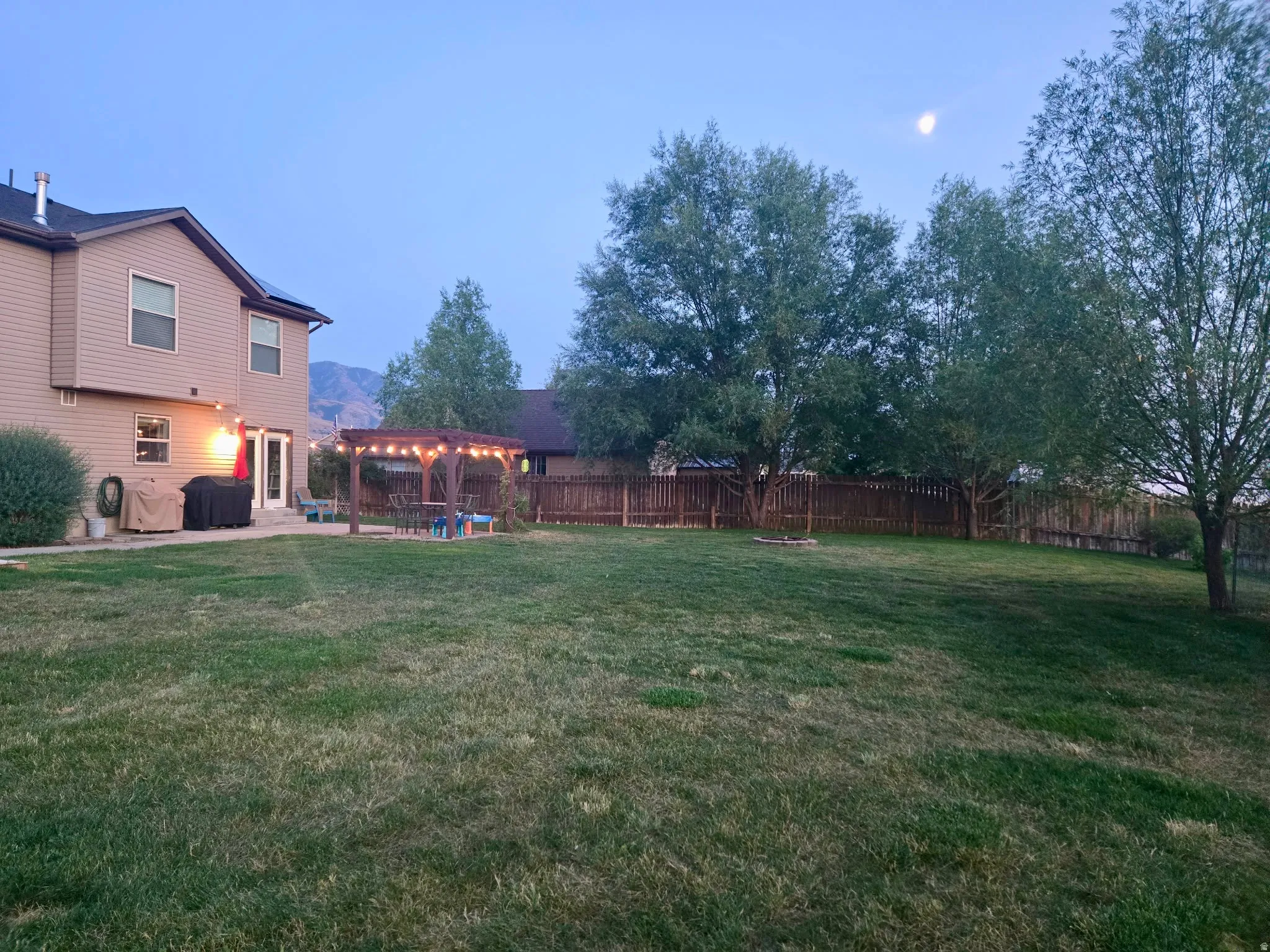 Expansive backyard featuring a lush lawn, mature trees, and a privacy fence