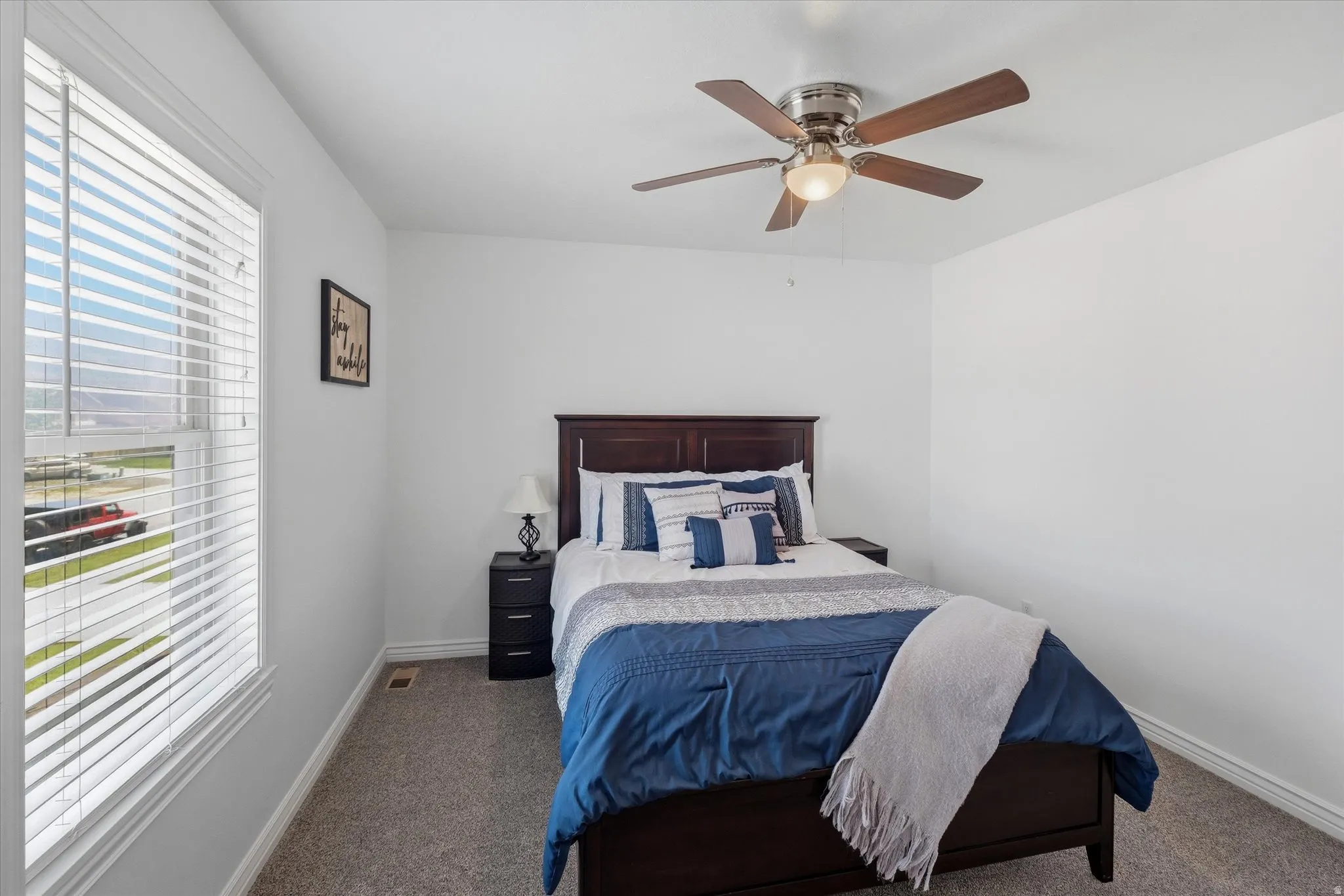 Bedroom featuring a ceiling fan with integrated lighting, a window with horizontal blinds, and neutral-toned carpeting