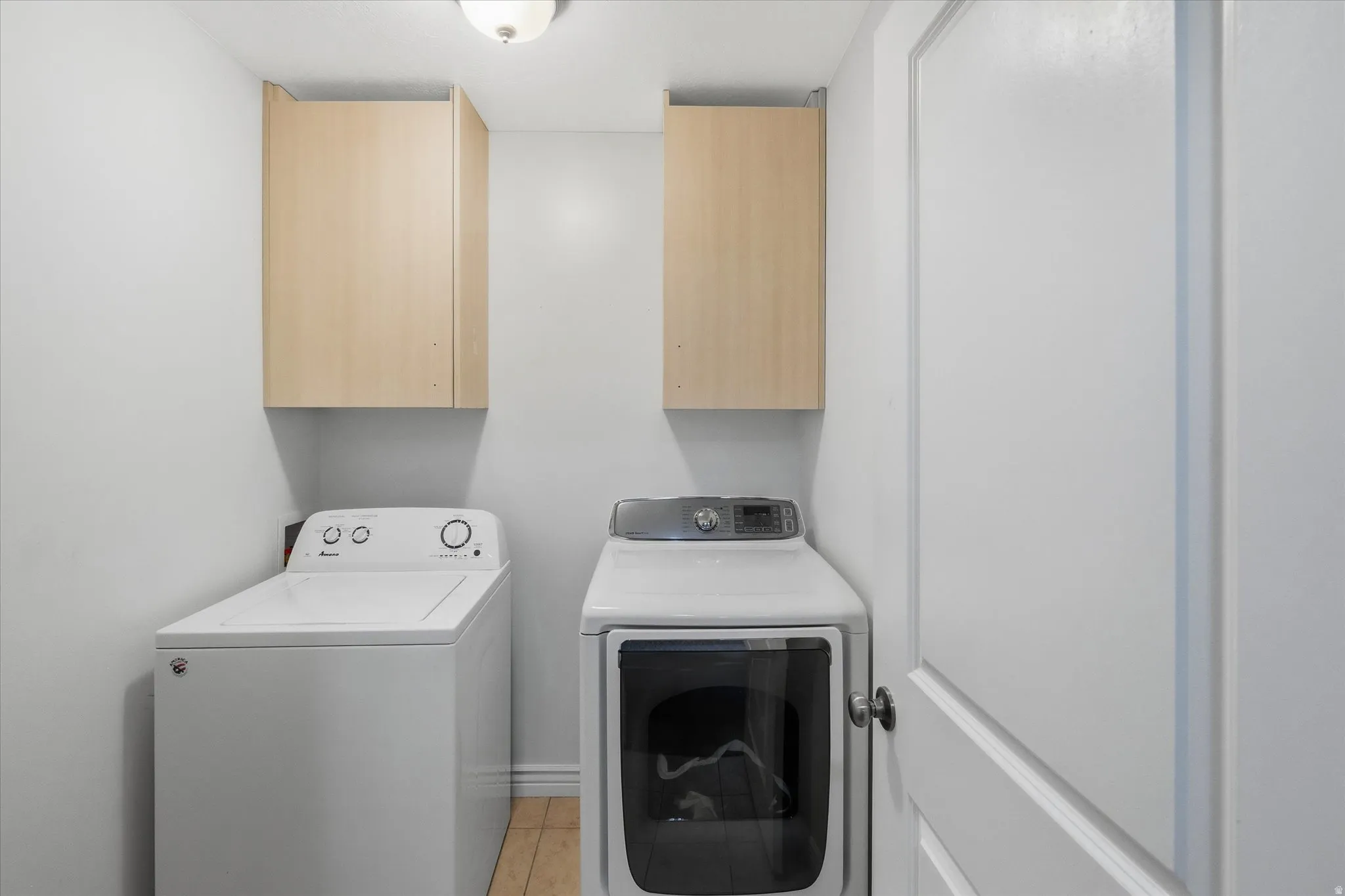 Dedicated laundry space with light wood-finish cabinetry, light plank flooring, and a white interior door with a black knob