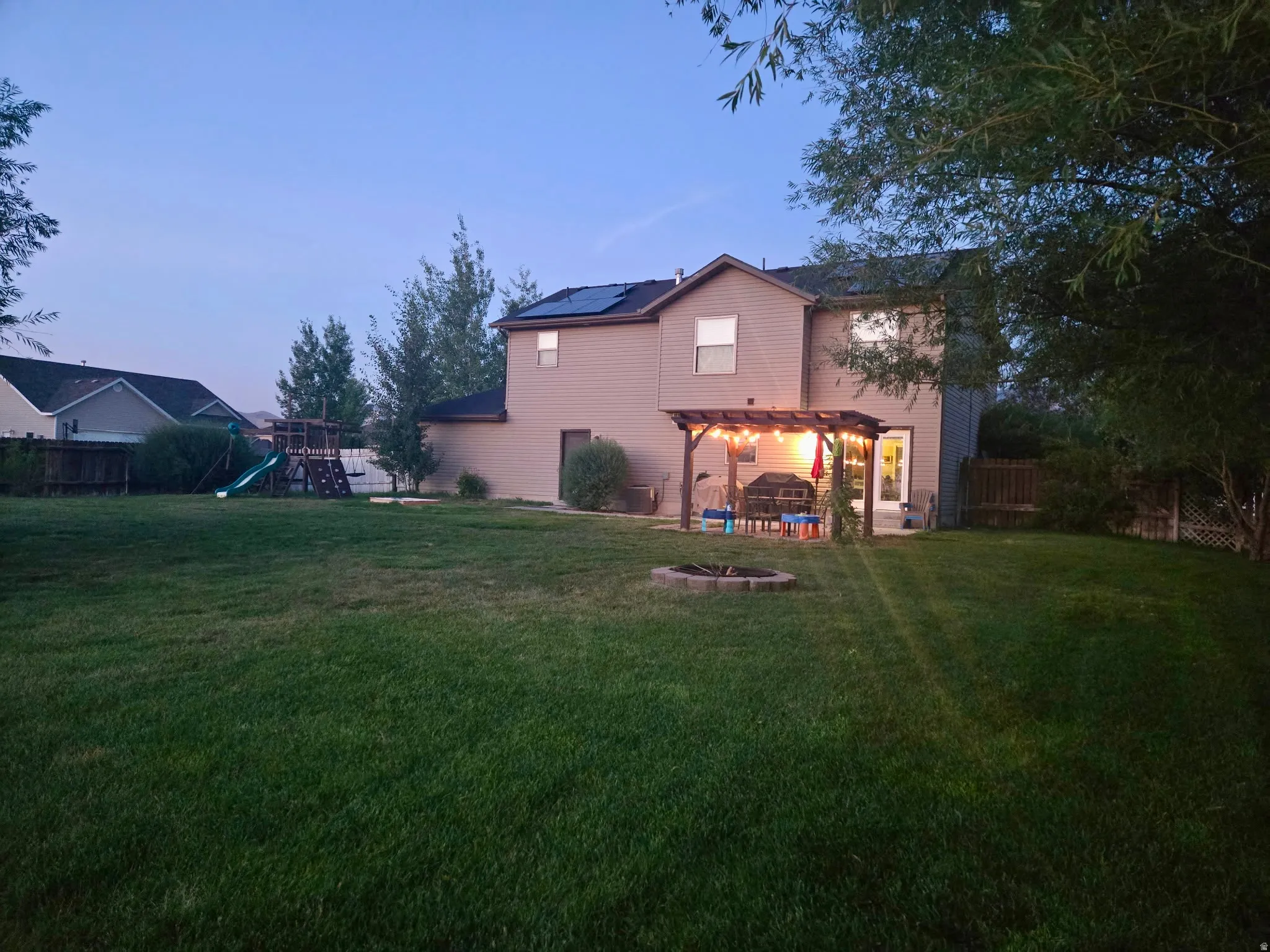 Expansive backyard featuring a manicured lawn, a fire pit, and a patio with a pergola