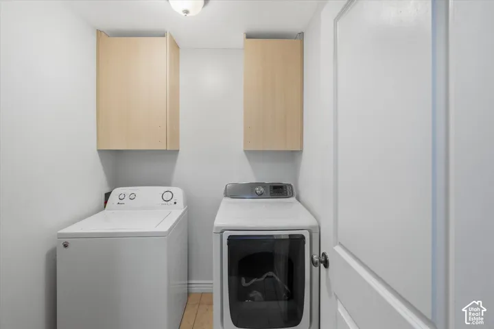 Dedicated laundry space with light wood-finish cabinetry, light plank flooring, and a white interior door with a black knob