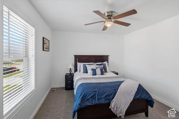 Bedroom featuring a ceiling fan with integrated lighting, a window with horizontal blinds, and neutral-toned carpeting