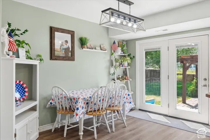 Dining area featuring wood-finish flooring, a contemporary linear chandelier, light green wall tones, and double glass-paneled doors leading to the exterior