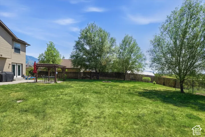 Expansive backyard featuring a large green lawn, mature trees, a wood pergola over a paved patio, and a privacy fence