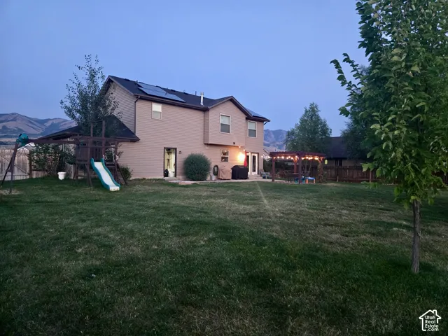 Expansive backyard featuring a large green lawn, a wooden playset, and a patio area with a pergola