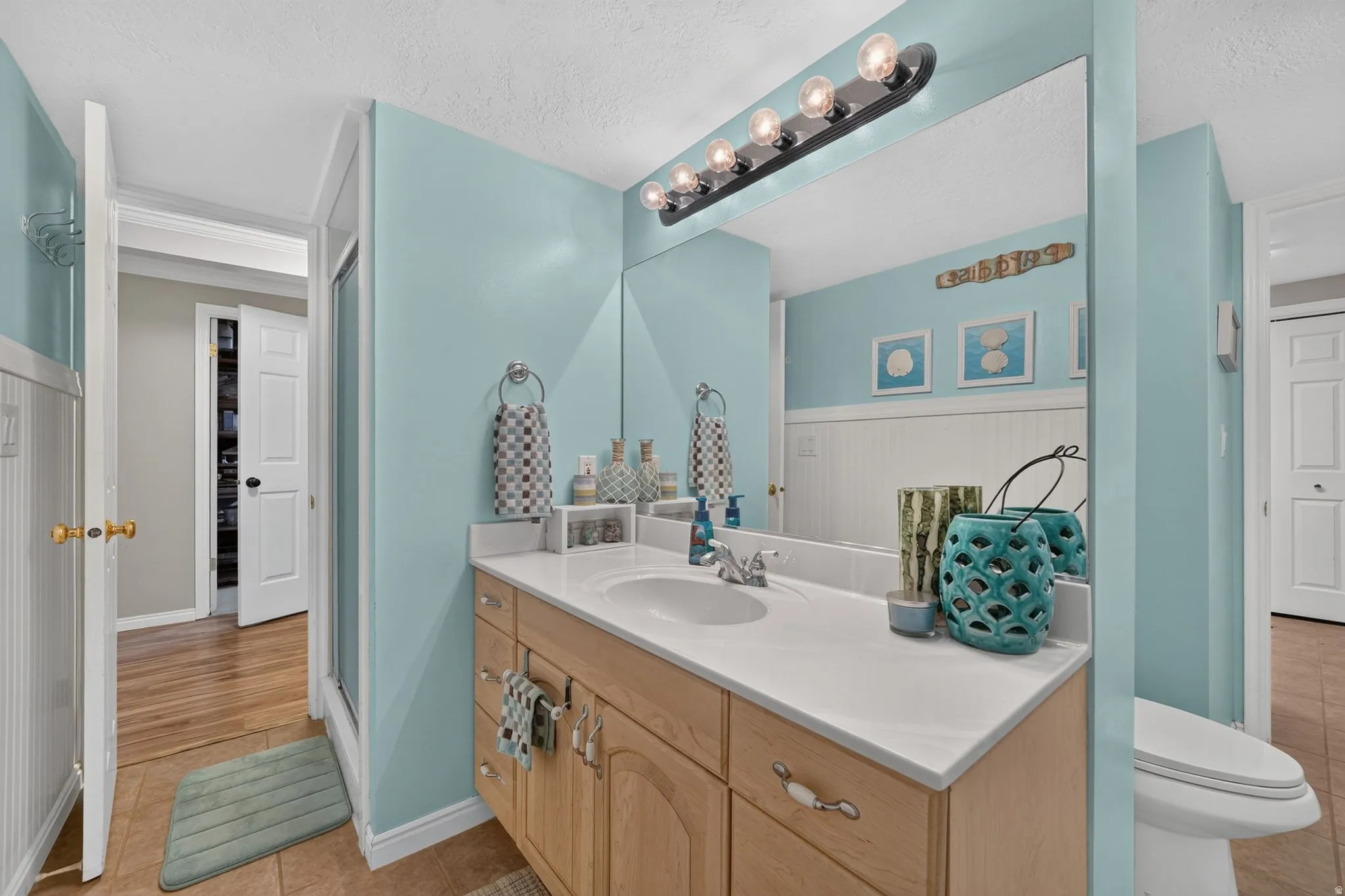 Bathroom vanity featuring a light wood-finish cabinet with white hardware, a white countertop, and an integrated sink