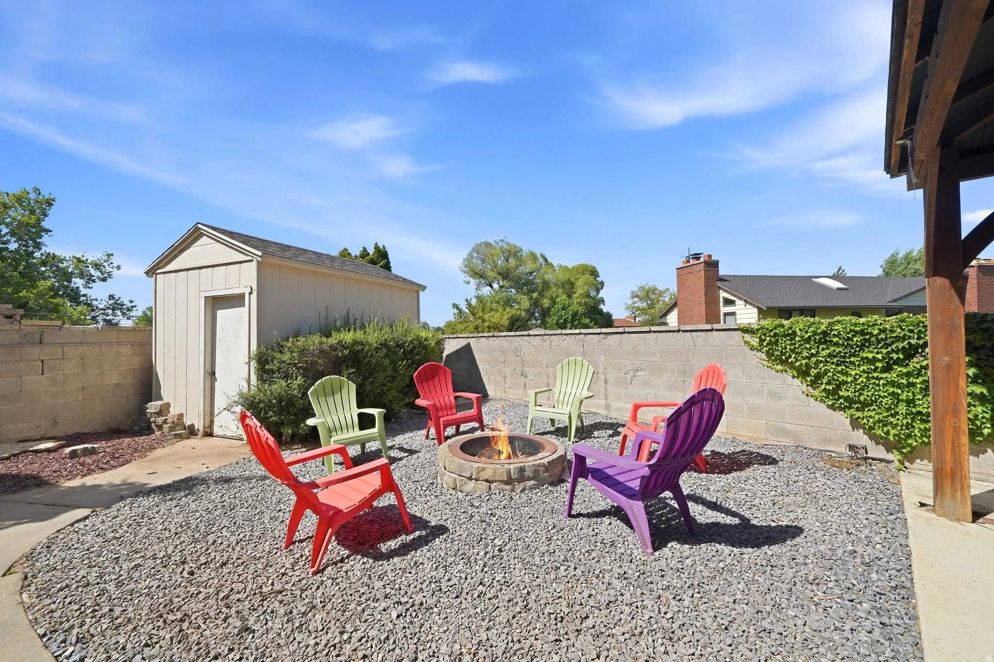 Gravel-covered patio area featuring a built-in fire pit, a block wall with climbing greenery, and an exterior storage shed