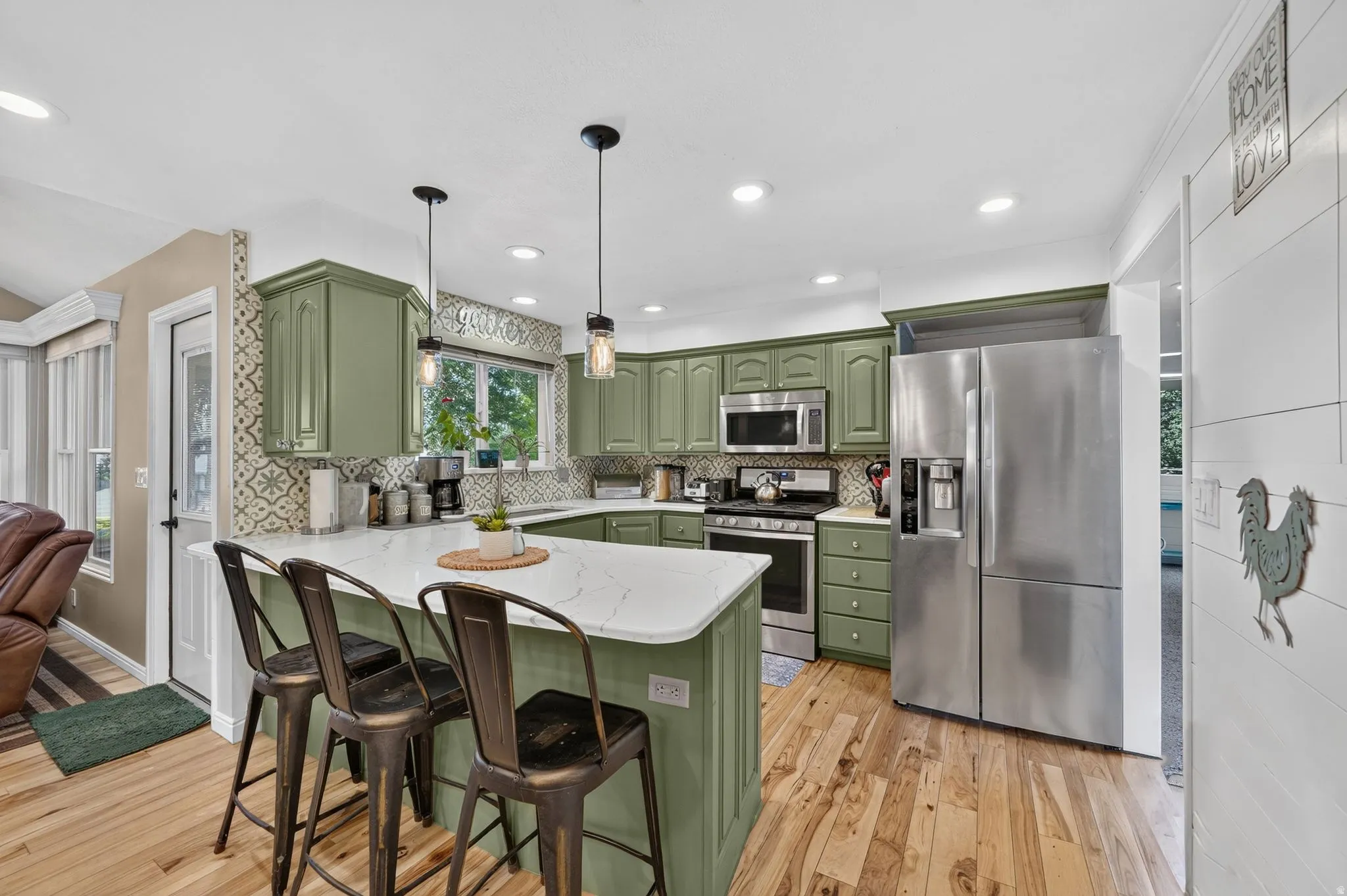 Kitchen featuring sage green cabinetry, stainless steel appliances, a white countertop island, pendant lighting, and wood-finish flooring