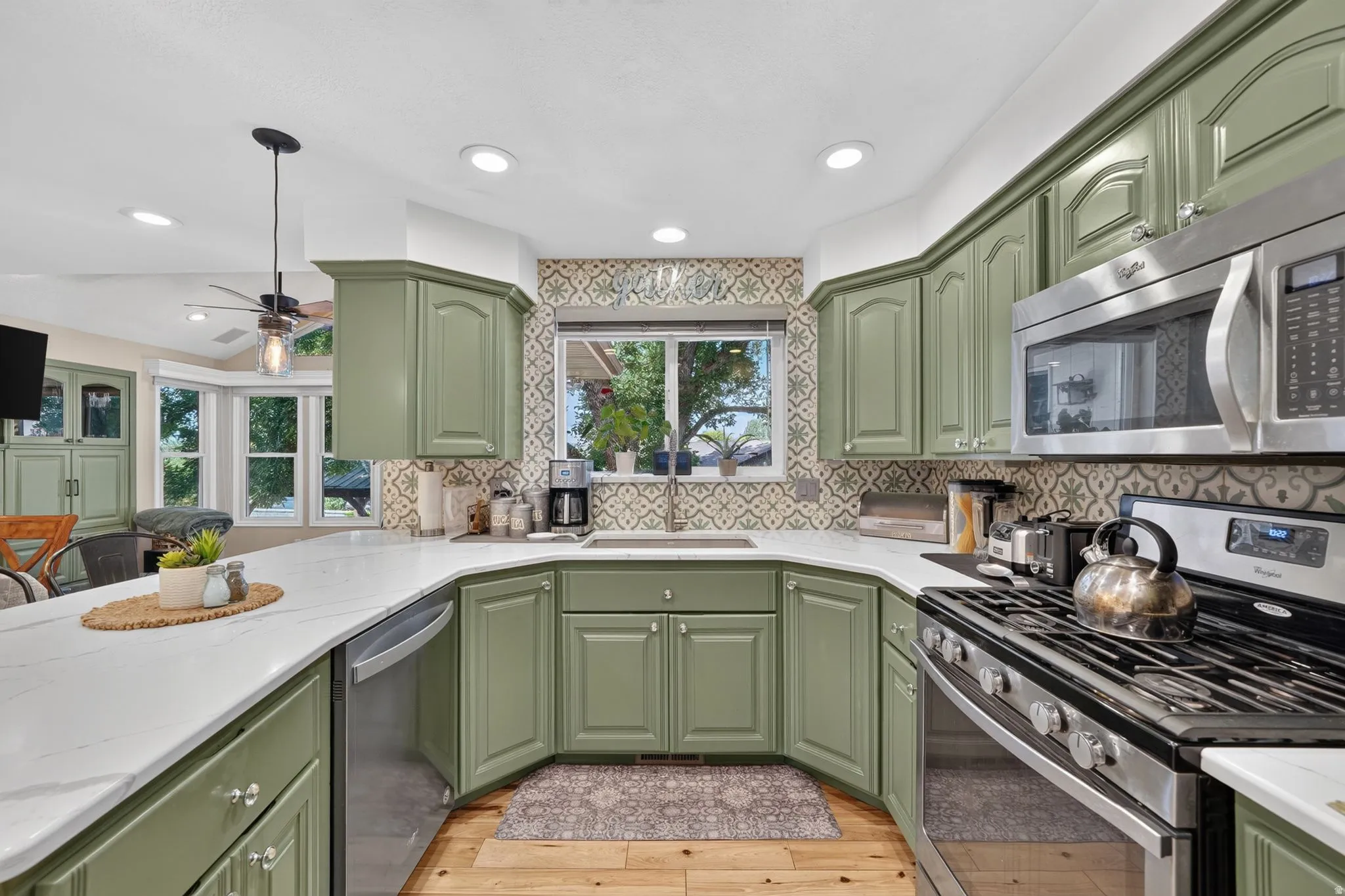 Kitchen featuring olive green cabinetry, stainless steel appliances, patterned tile backsplash, white countertops, and wood-finish flooring