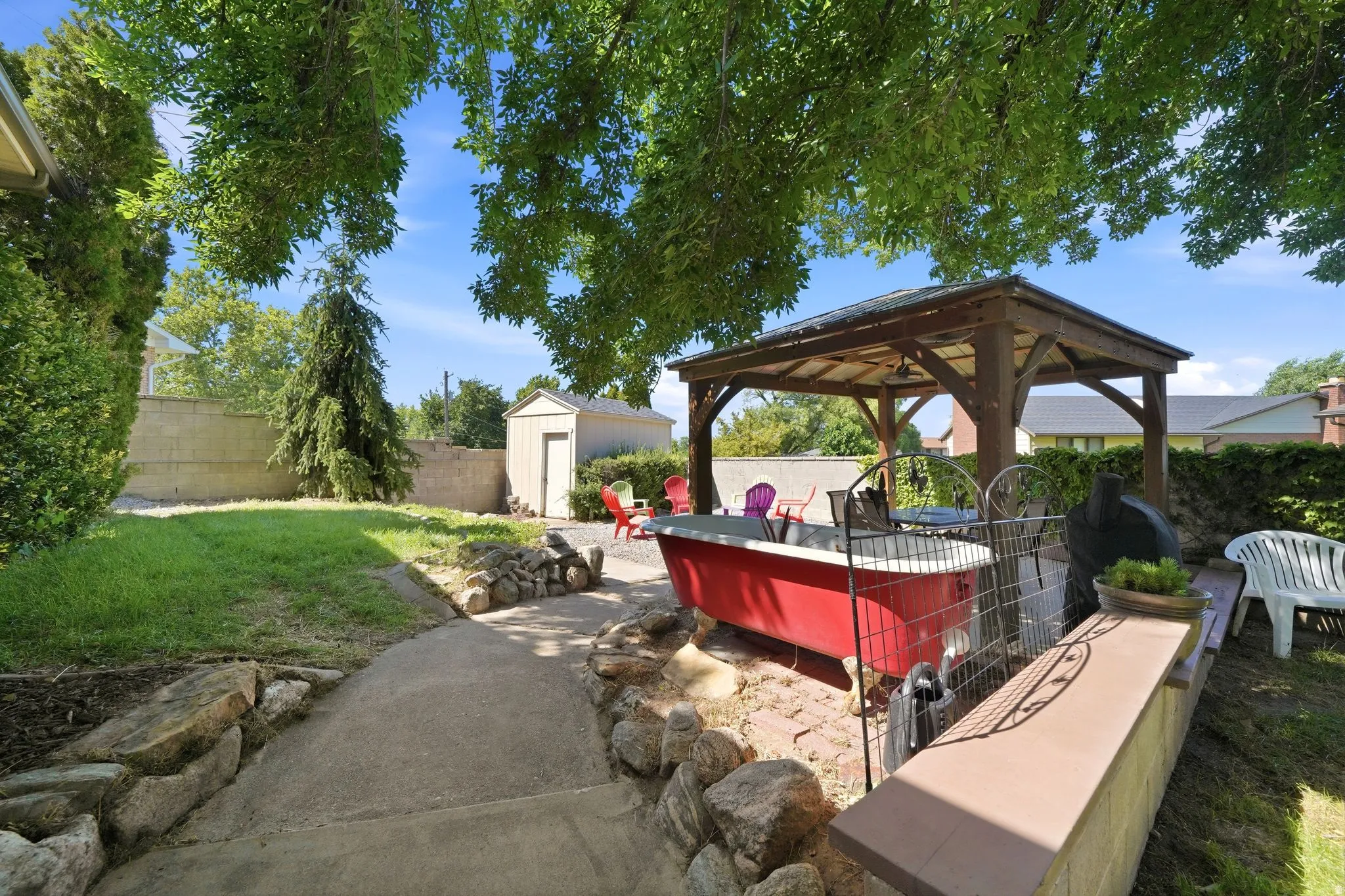 Spacious backyard featuring a stone-edged concrete pathway, a wood-framed gazebo over a brick patio, a concrete block privacy fence, and a white storage shed