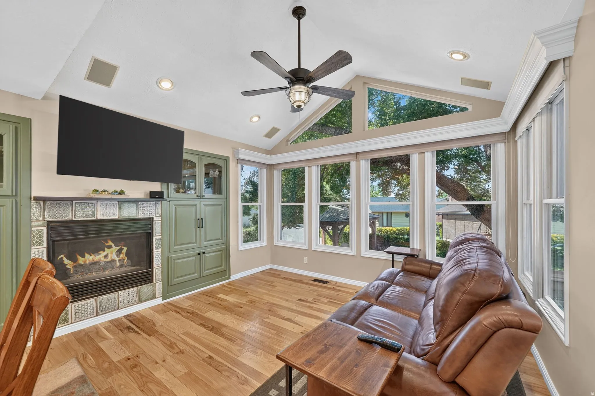 Living area featuring wood-finish flooring, a fireplace with tiled surround, built-in cabinetry, and expansive windows with transom accents